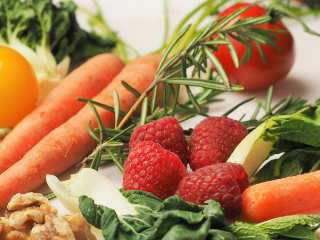 A selection of healthy fruit and vegetables, including carrots, raspberries, tomatoes and green leaves